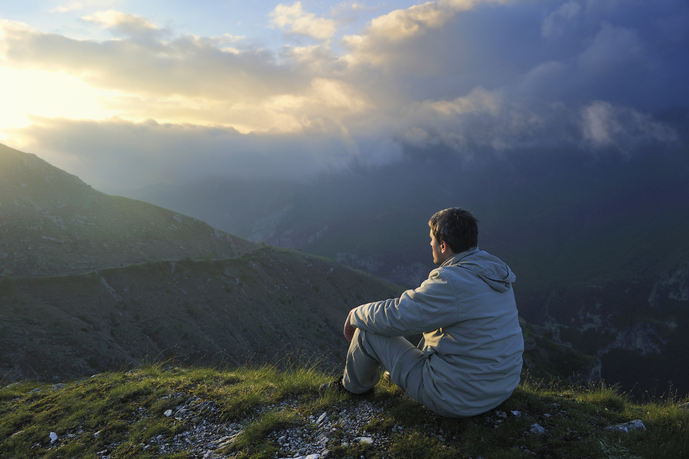 A man sits outdoors in a peaceful setting